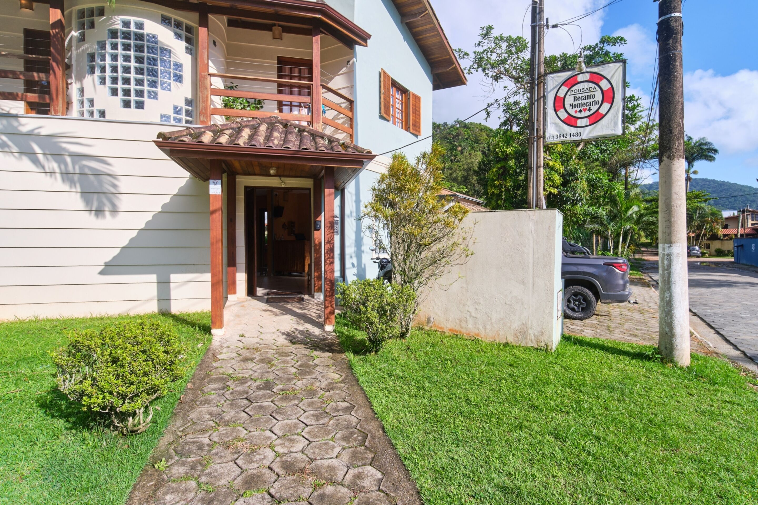 Um edifício de dois andares com entrada coberta de azulejos, um pequeno jardim e um carro estacionado.