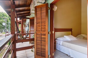 A wooden-framed room with a bed, a hammock, and a view of a staircase leading outside. - Pousada Recanto Montecarlo (Ubatuba)