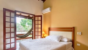 Un dormitorio con cama, una hamaca, una mesita de noche con lámpara y un equipo de aire acondicionado.