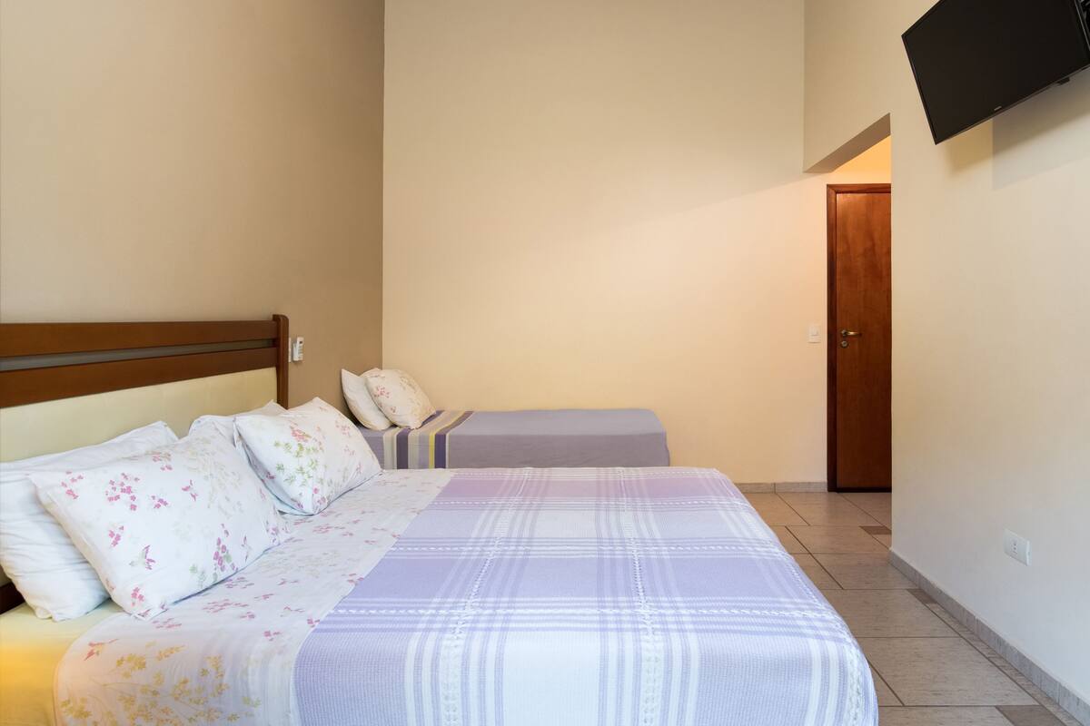 A bedroom with two beds, a wooden headboard, a flat-screen TV mounted on the wall, and a door in the background.