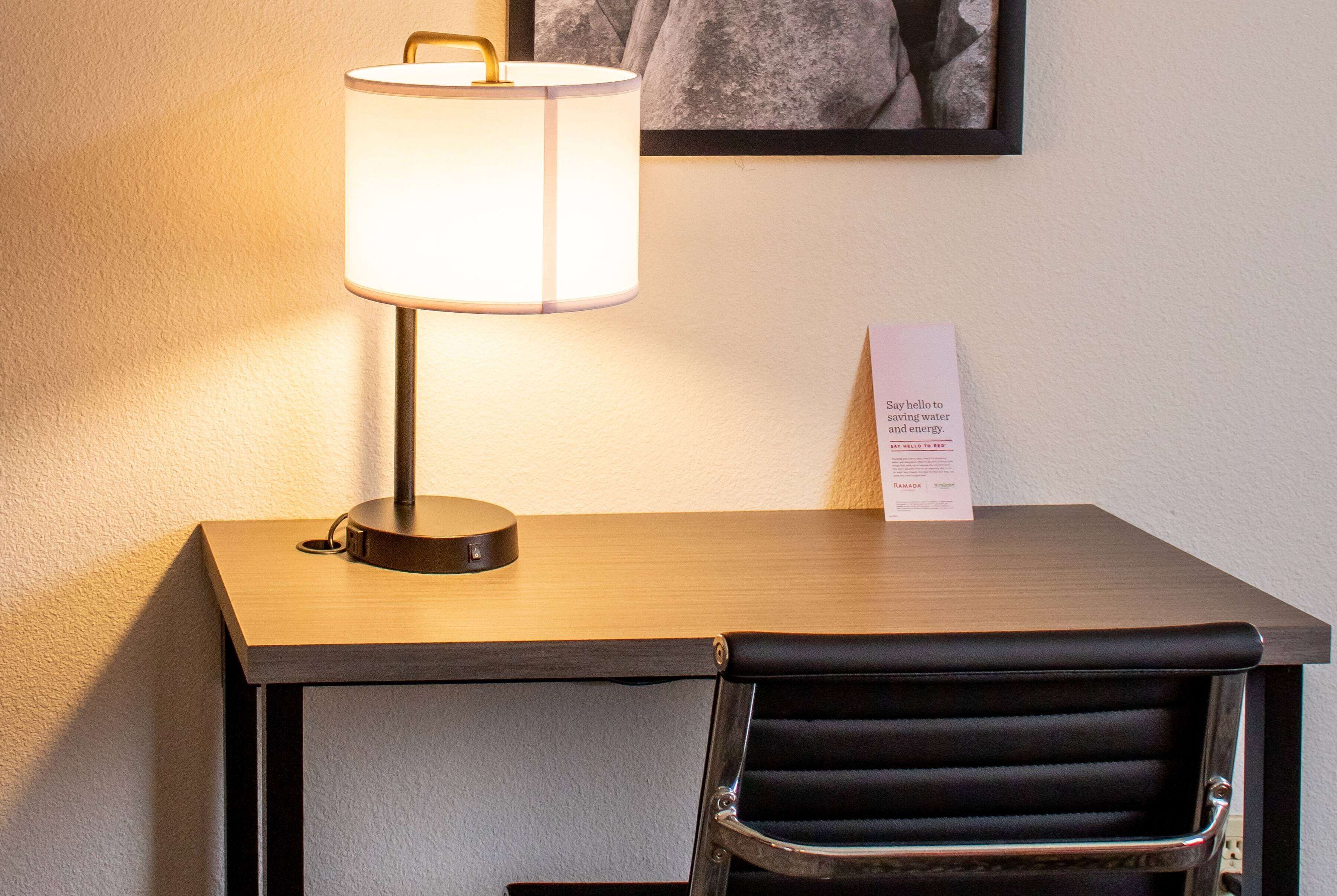 Ein Schreibtisch mit Lampe, ein Stuhl und ein gerahmtes Bild an der Wand.