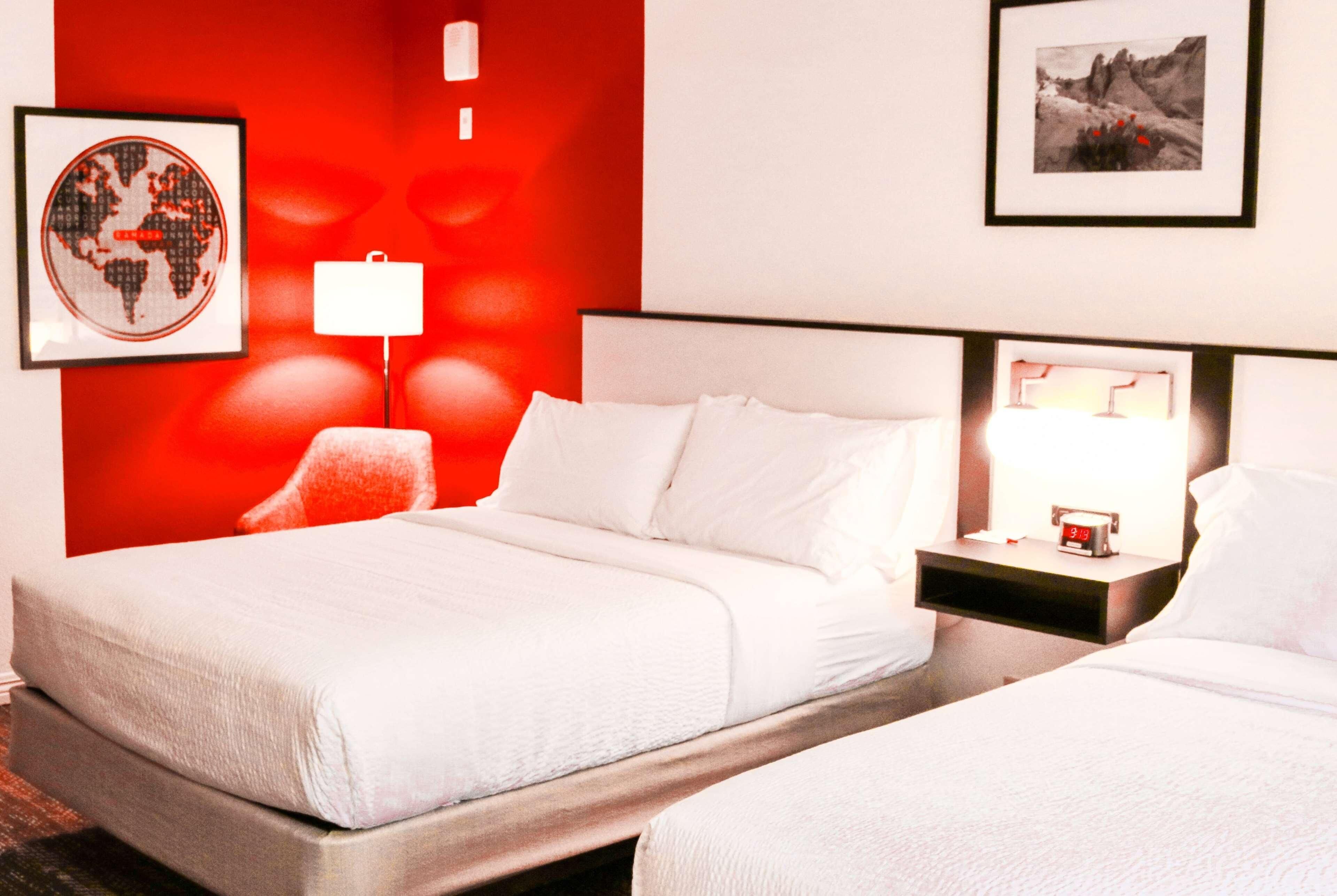 A hotel room with a large bed, a bedside table with a lamp, a framed world map, and a framed picture on the wall.