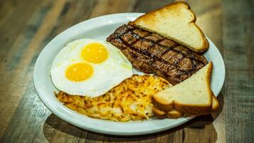 Un plato con dos huevos fritos, una porción de bistec a la parrilla, patatas ralladas y dos tostadas.