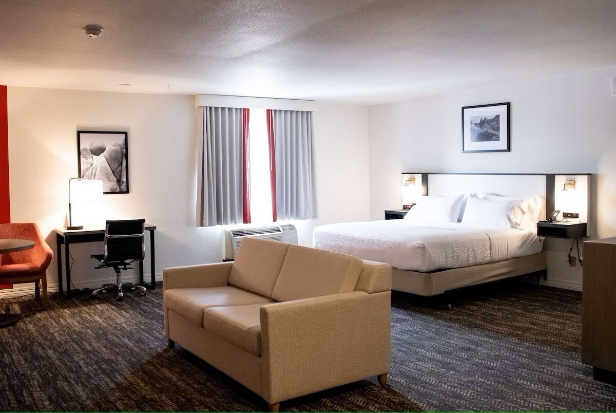 A hotel room with a bed, a desk, a chair, a lamp, and a picture on the wall.