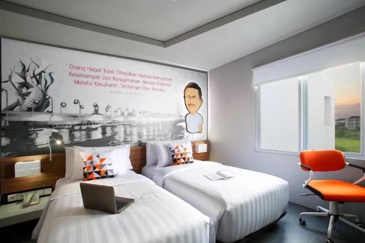 A hotel room with two beds, a laptop on one bed, a chair, and a large window.