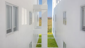 A modern building with white exterior walls, multiple windows, and a central open space leading to a grassy area. - Berry Biz Hotel Powered by Archipelago (Legian)
