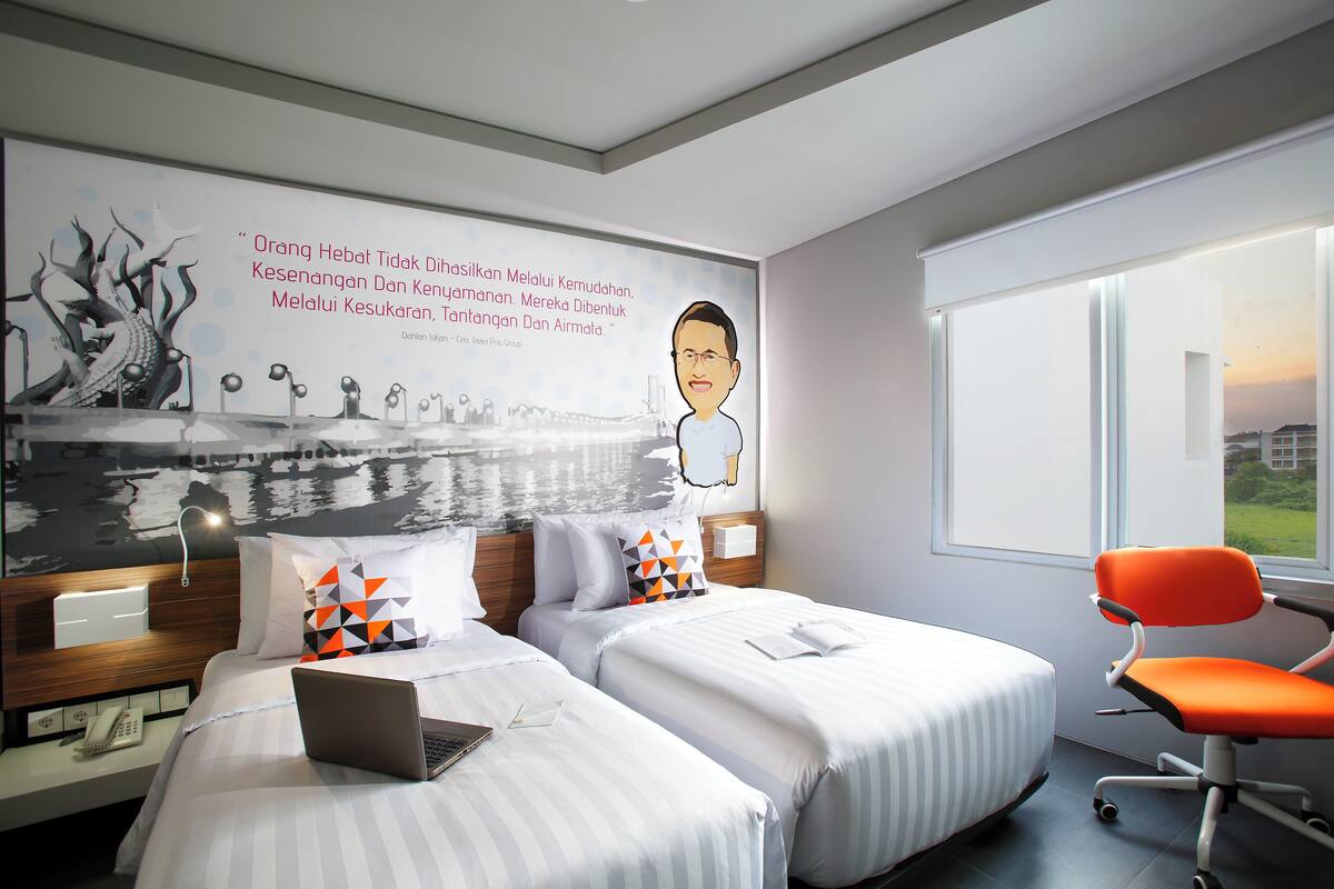 A hotel room with two beds, a laptop on one bed, a chair, and a large wall mural.