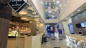 A modern coffee shop with a sign reading "BROWN & BUTTER COFFEE SHOP" in a spacious, well-lit interior with a high ceiling and contemporary design elements. - Berry Biz Hotel Powered by Archipelago (Legian)