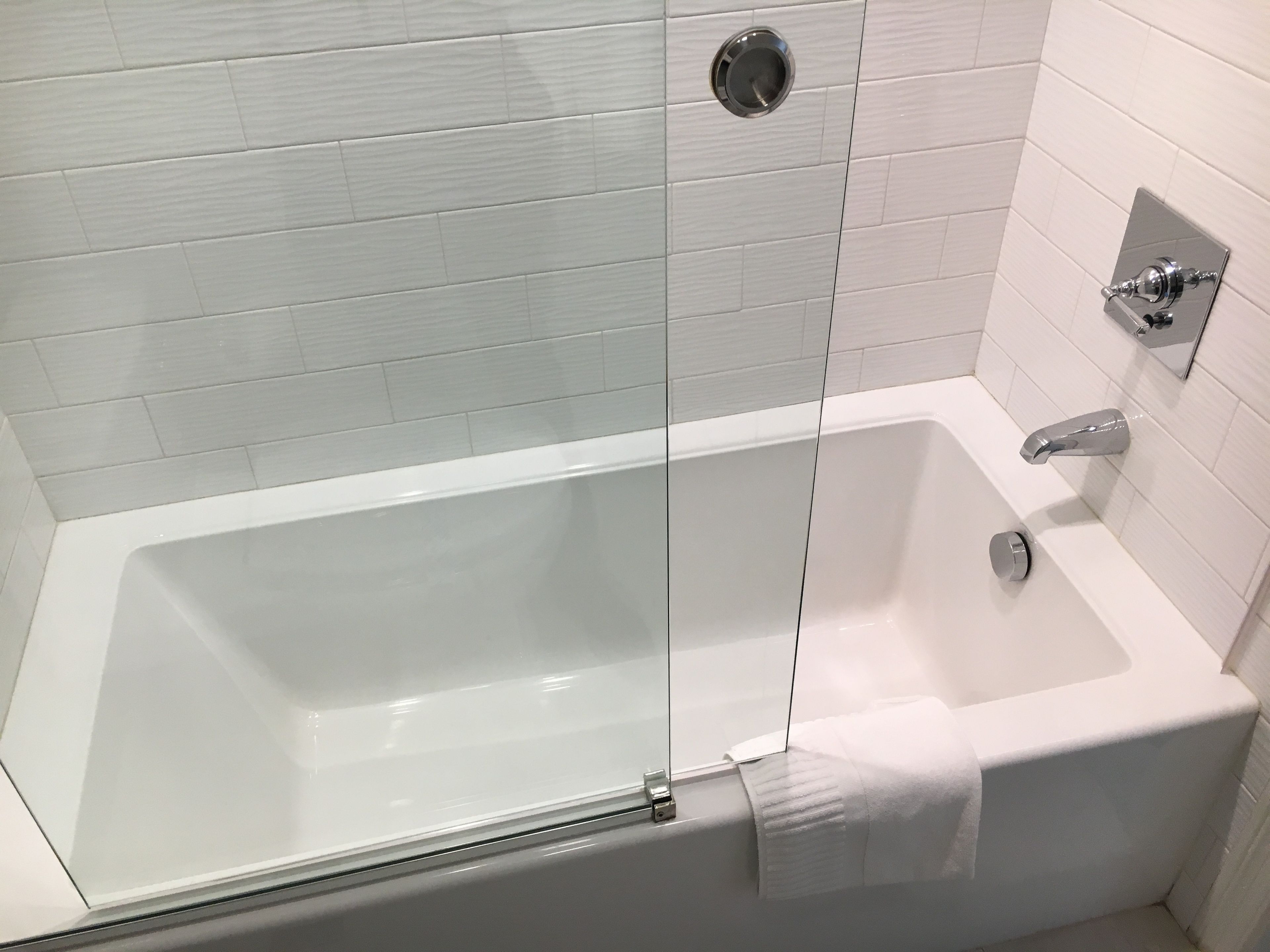 A modern bathroom with a glass-enclosed bathtub, a handheld showerhead, and a towel rack.