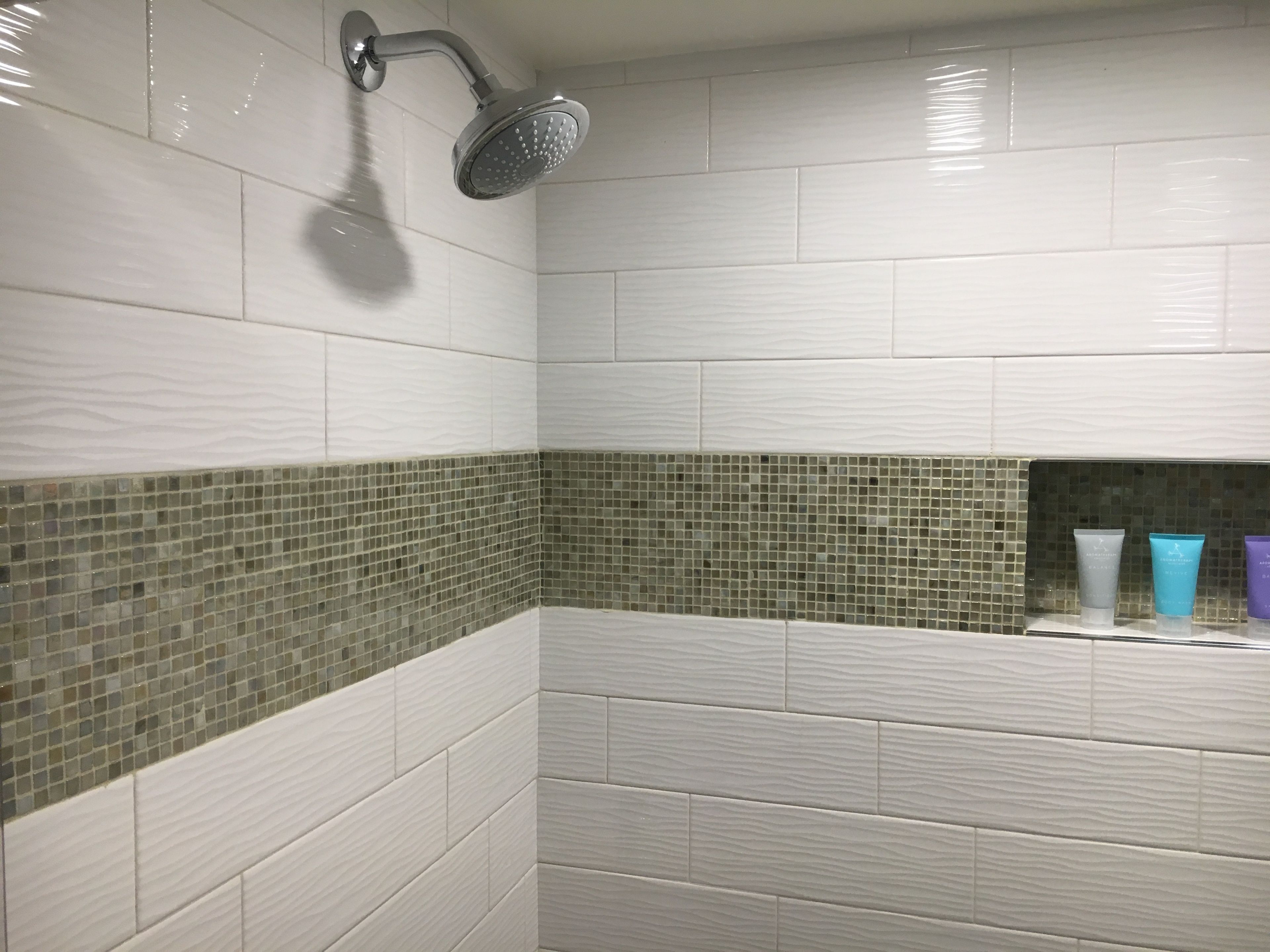 Un baño con azulejos blancos tipo metro, una ducha con cabezal de ducha manual y un estante con tres recipientes de tocador.