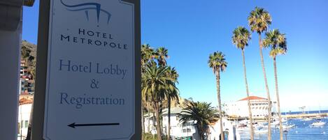 A sign for the Hotel Metropole's lobby and registration area, with a view of the marina and palm trees in the background.