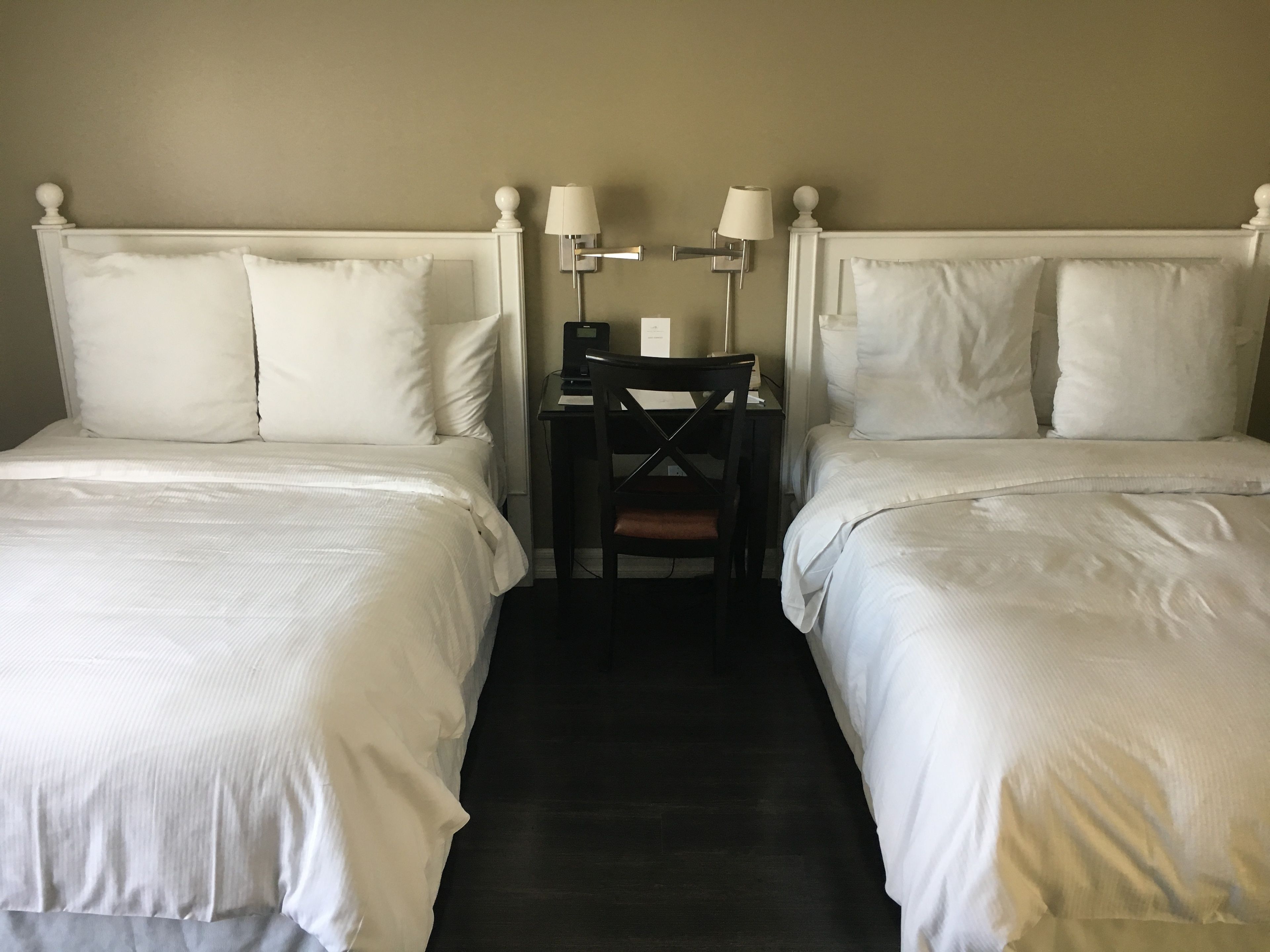 Habitación de hotel con dos camas individuales, una mesita con una silla y dos lámparas de pared.