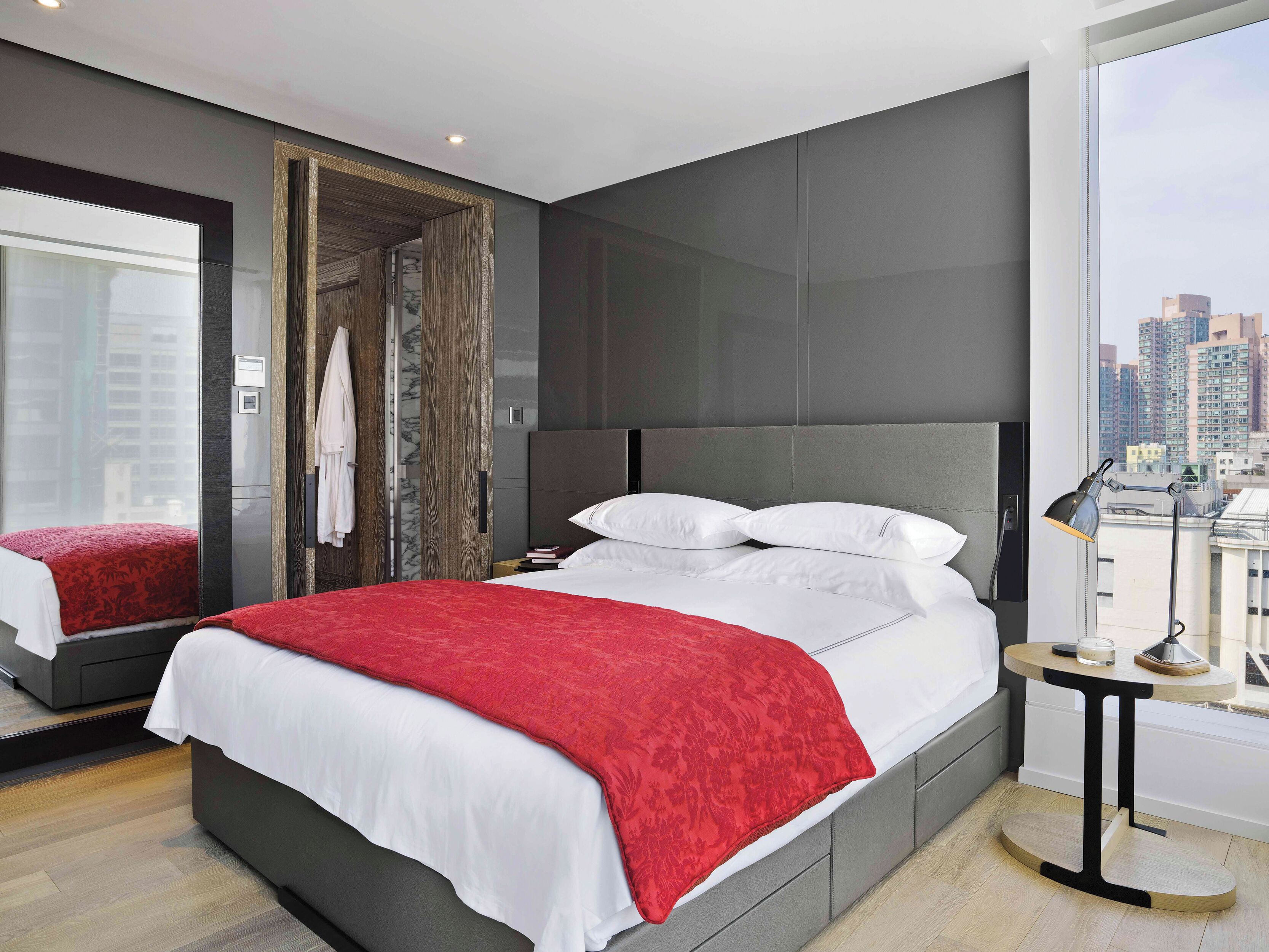 A modern hotel room with a large bed, a bedside table, a mirror, and a city view.