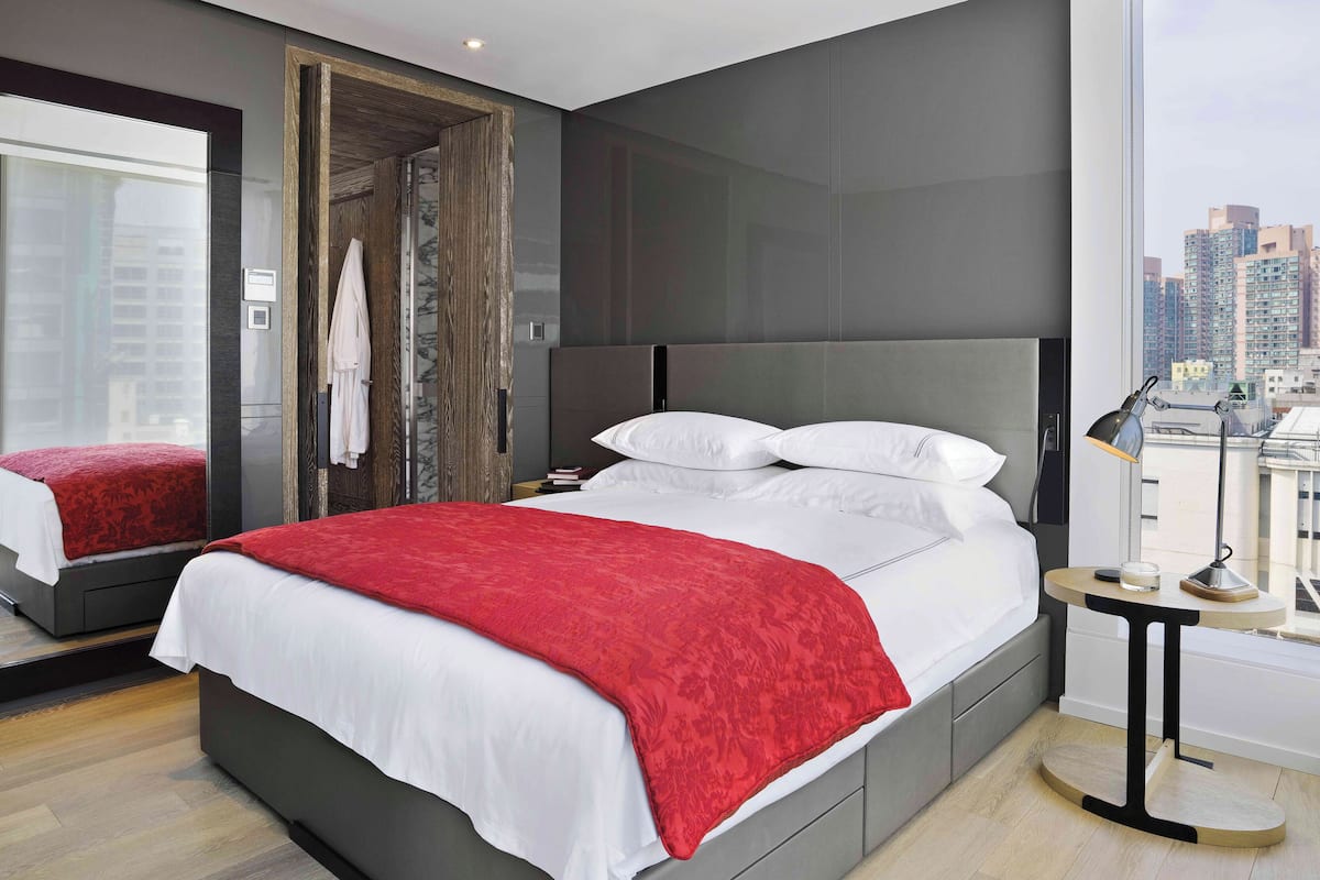 A modern hotel room with a large bed, a bedside table, a mirror, and a city view.