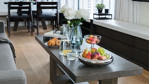 Ein Essbereich mit einem Holztisch, gedeckt mit einer Obstschale, Croissants, einer Blumenvase und einer Kaffeemaschine.