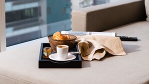 Ein modernes Wohnzimmer mit einer Couch, einem Tablett mit einem Croissant, einer Tasse und einer Fernbedienung.