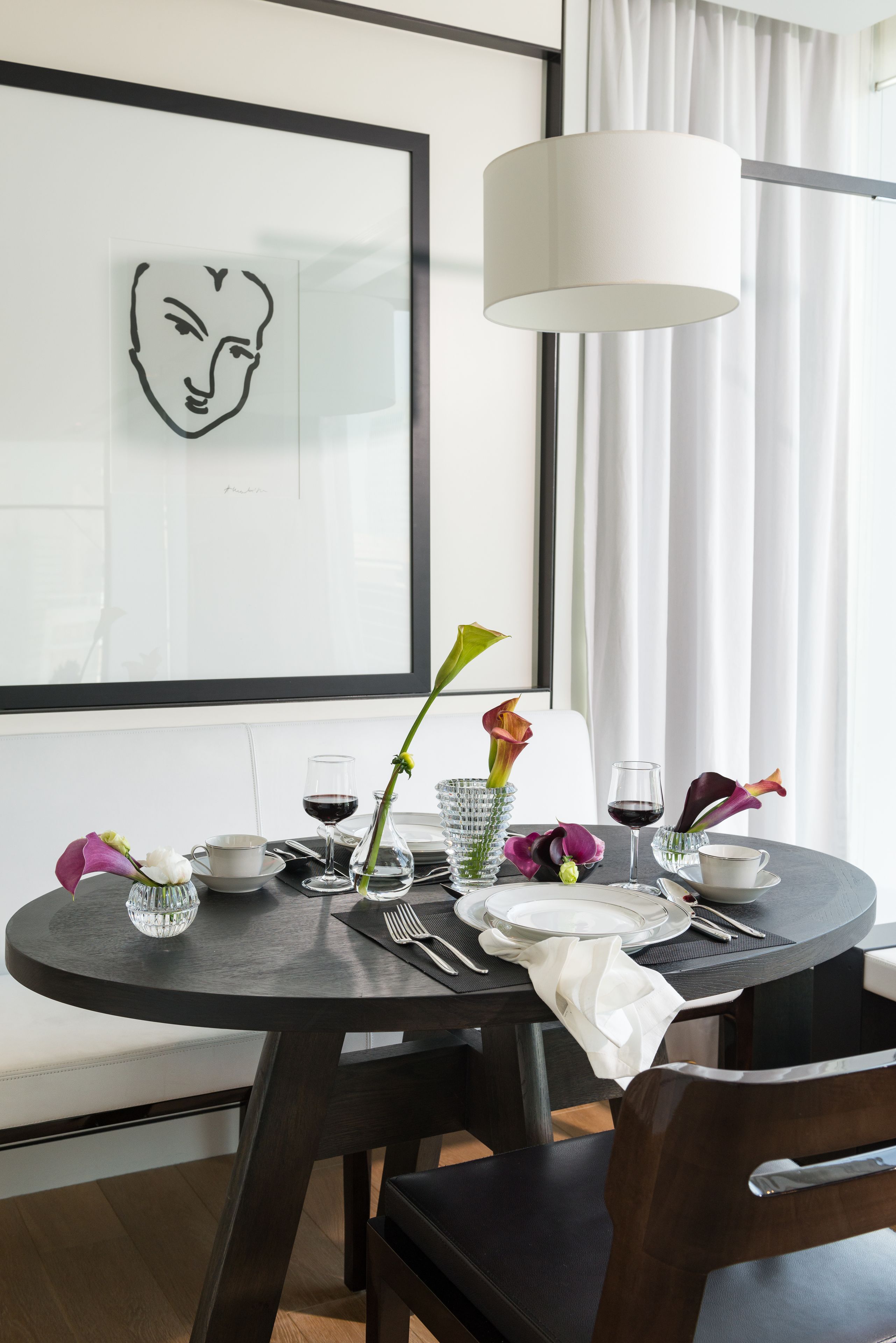 A dining table set with a white tablecloth, a vase with flowers, a wine glass, and a framed artwork on the wall.