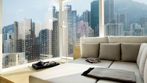 Ein modernes Wohnzimmer mit großem Fenster und Blick auf die Stadt, einer Couch mit Kissen, einem Tablett mit Teekanne und Tasse sowie einem Buch auf der Couch.