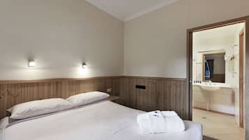 A hotel room with a wooden headboard, two beds with white linens, a bathroom with a sink and mirror, and a towel on the bed.