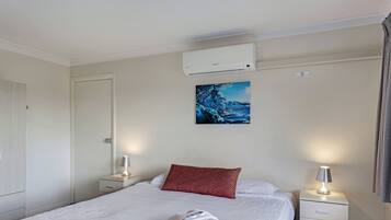 Une chambre d’hôtel avec un lit, un oreiller rouge, une serviette blanche, une table de chevet avec une lampe et un climatiseur fixé au mur.