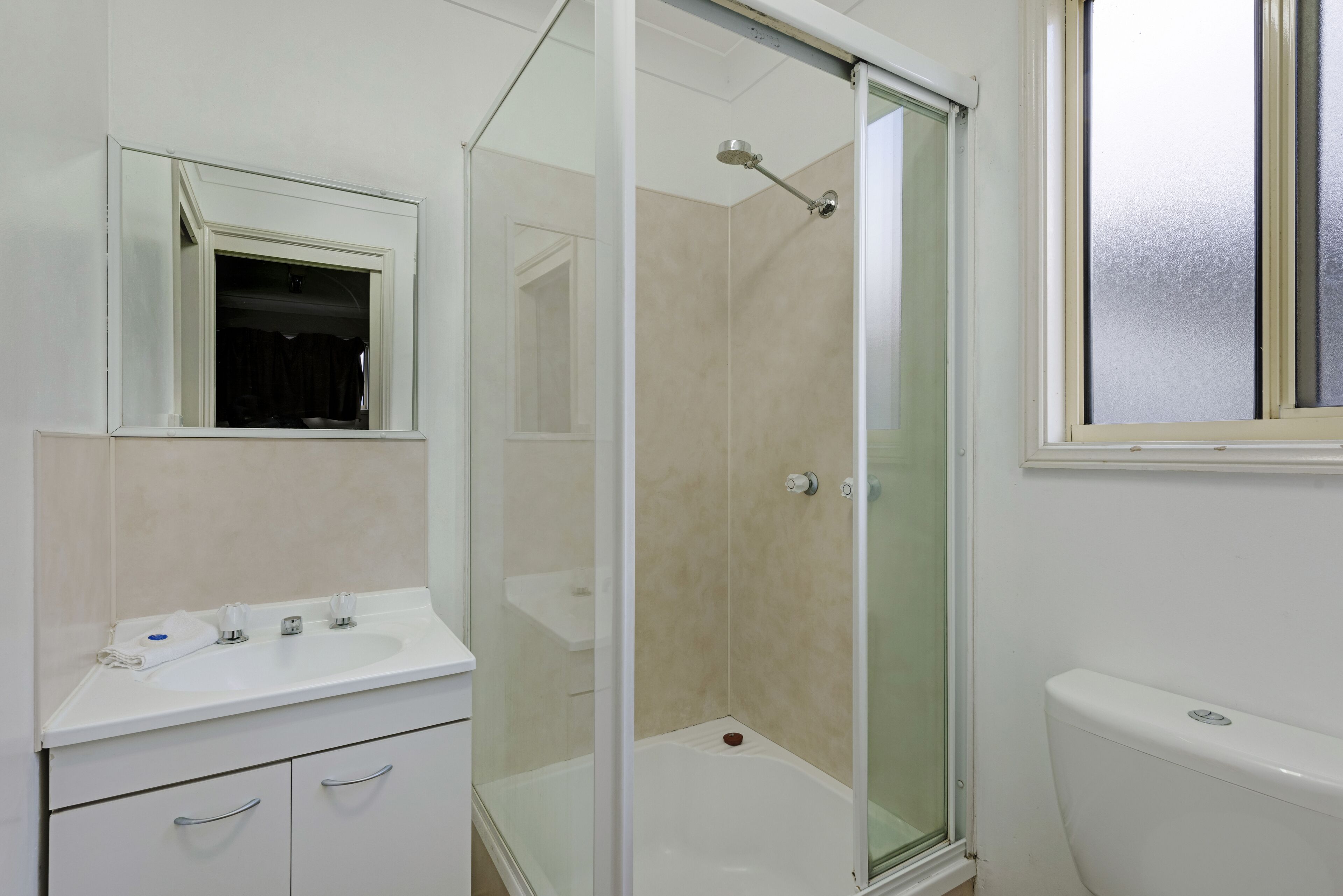 Un baño con ducha acristalada, lavamanos blanco y un inodoro.