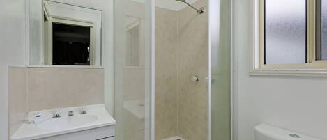 Un baño con ducha acristalada, lavamanos blanco y un inodoro.