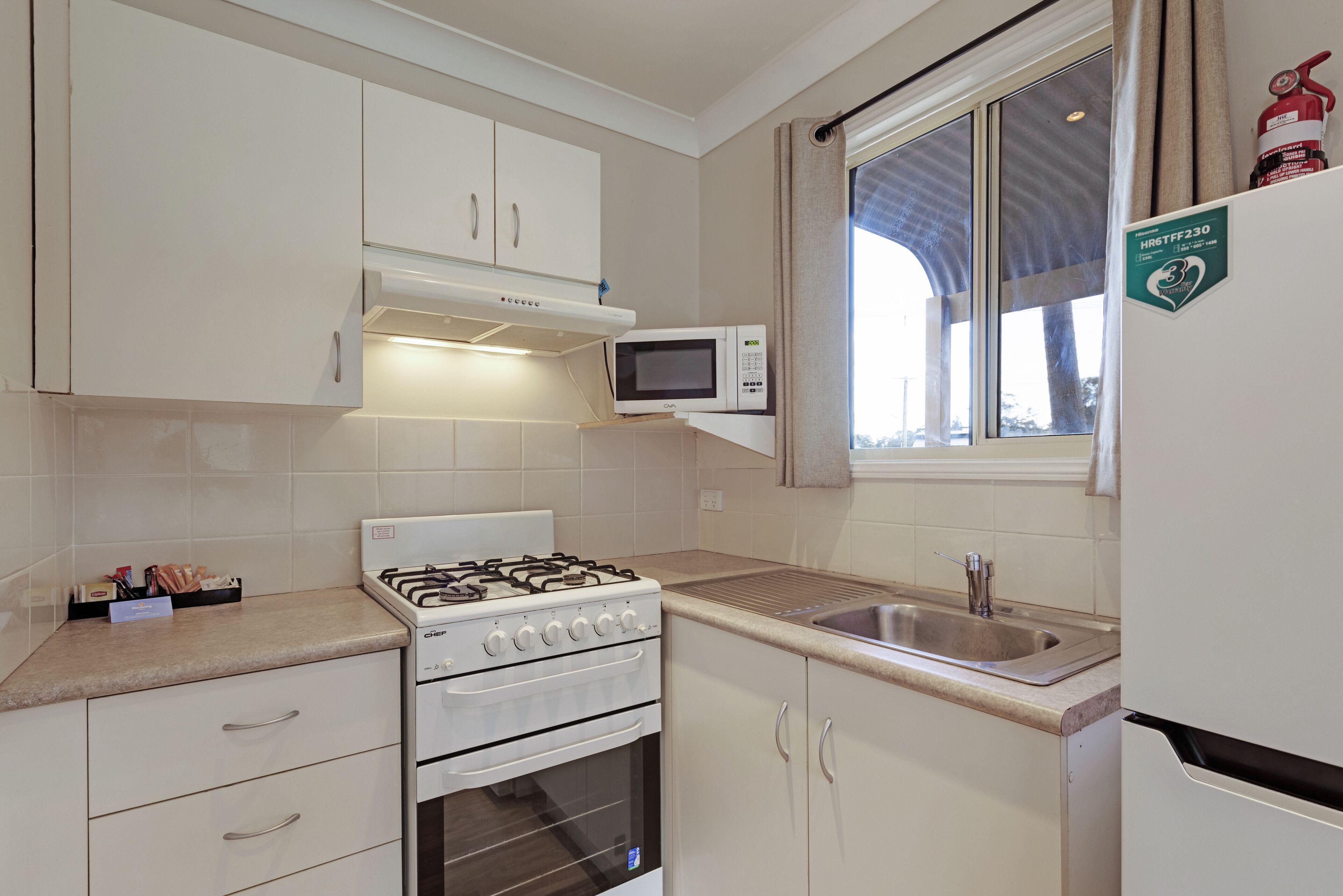 A compact kitchen with white cabinets, a gas stove, a microwave, and a sink.