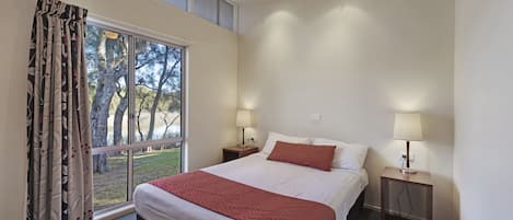 A bedroom with a large bed, two bedside tables with lamps, a window with curtains, and a ceiling fan.