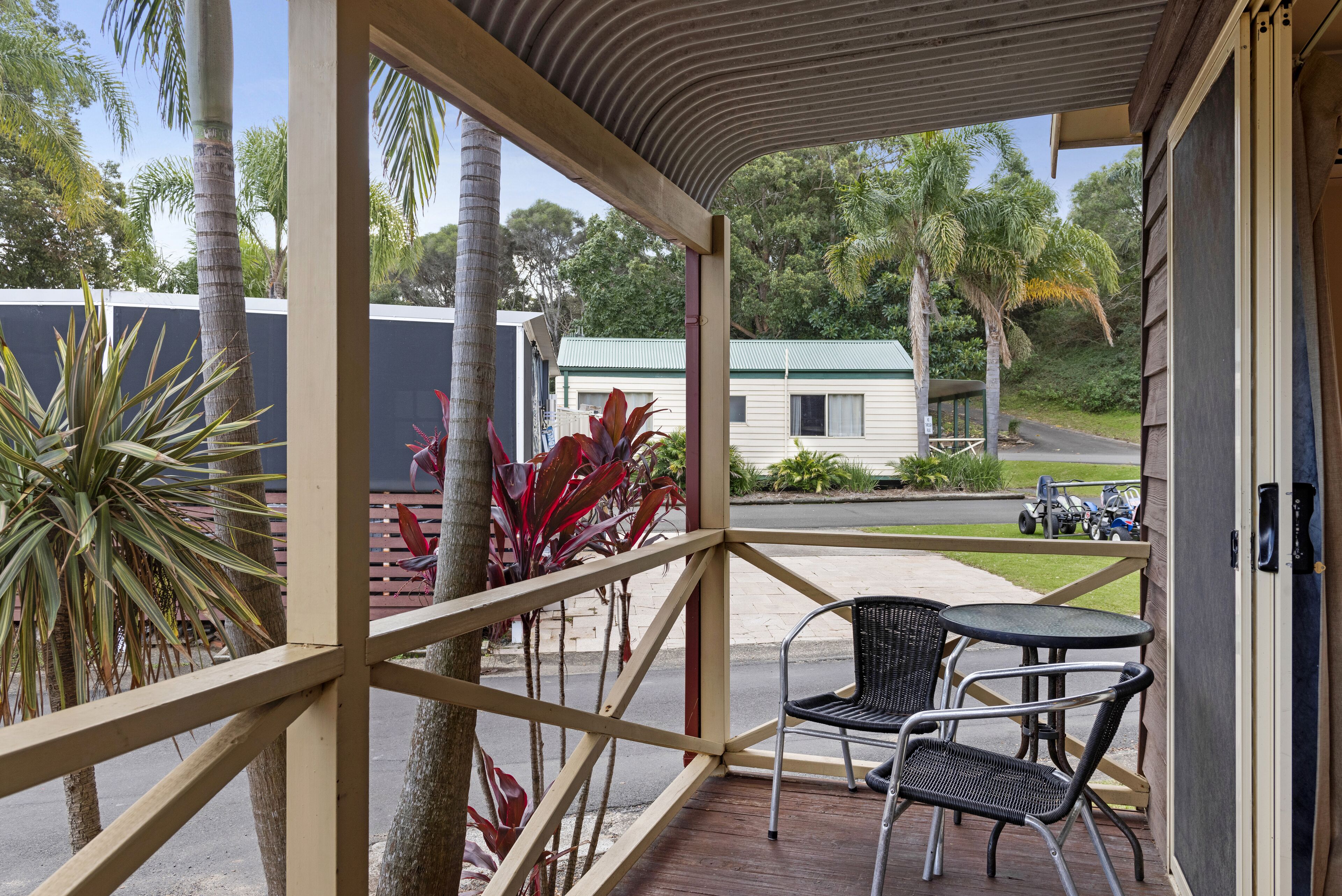 A covered outdoor seating area with a table and chairs, surrounded by palm trees and plants.