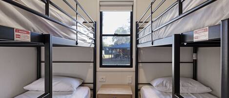 A dormitory room with bunk beds, a small wooden table, and a window with a view of the outside.