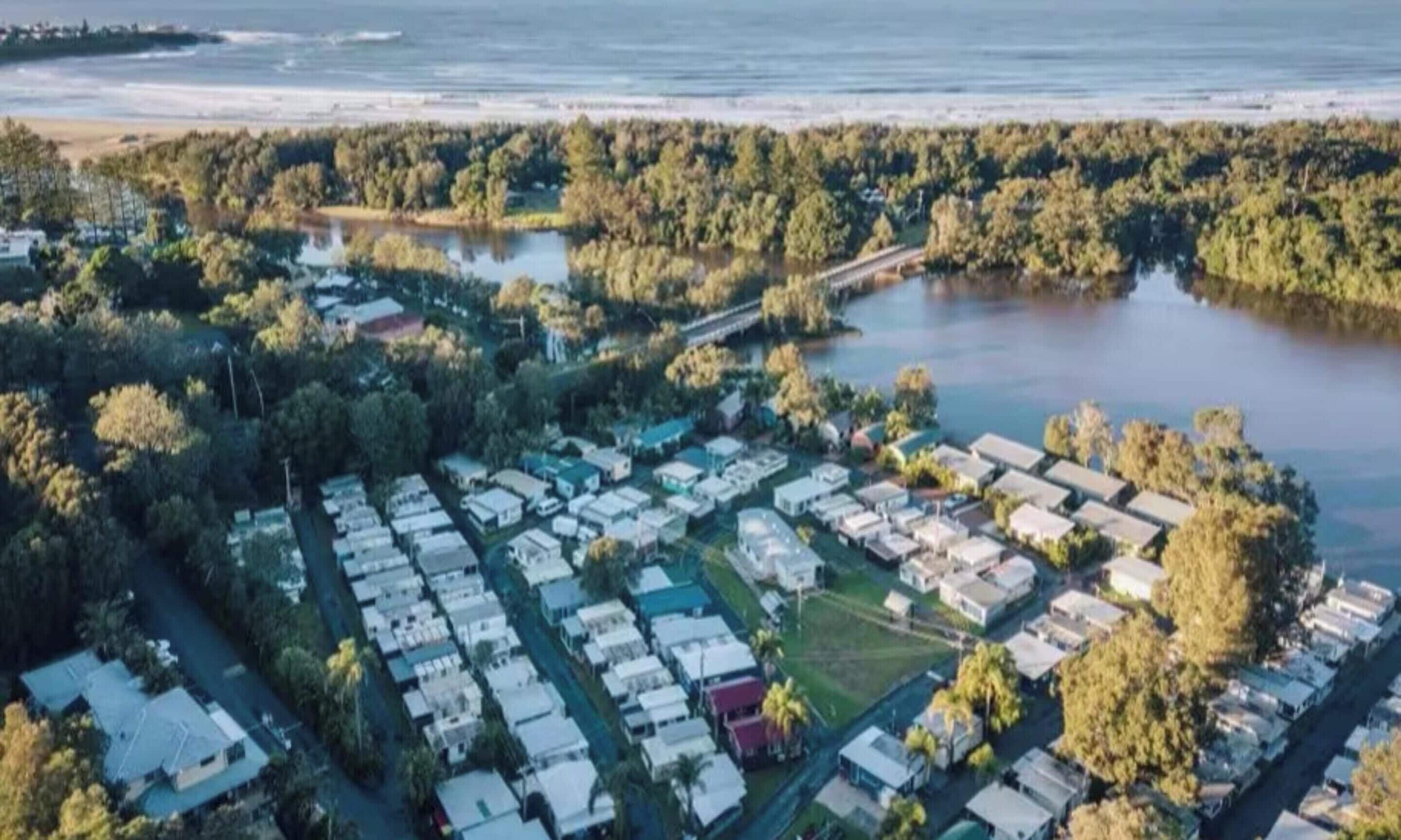 An aerial view of a campground with RVs and cabins, a lake, and a forested area.