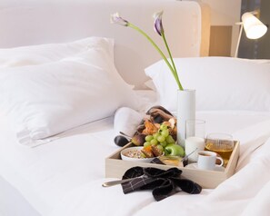 A neatly made breakfast tray on a bed with a book, a vase with flowers, and a lamp in the background.