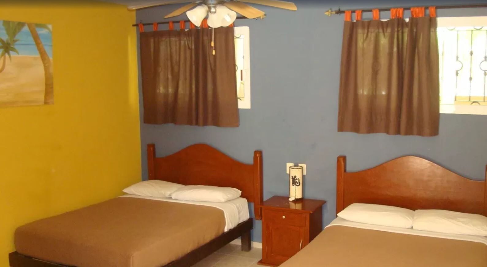 Una habitación con dos camas, ventilador de techo y cortinas.
