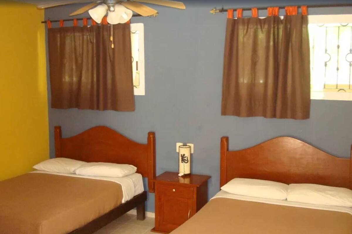 A room with two beds, a ceiling fan, and curtains.