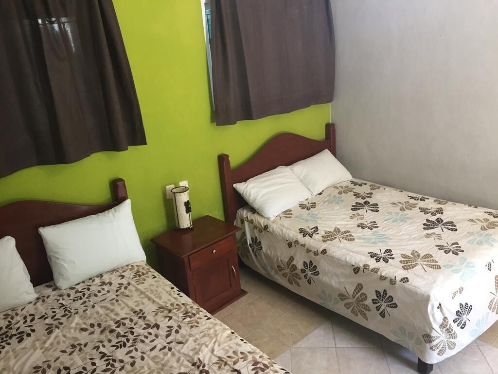 Una habitación con dos camas, una mesita de noche y una ventana con cortinas.
