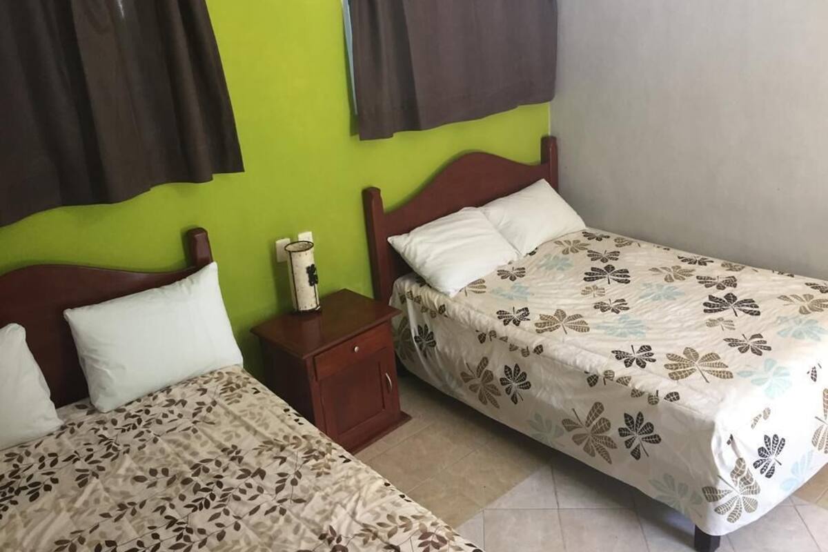 A room with two beds, a nightstand, and a window with curtains.