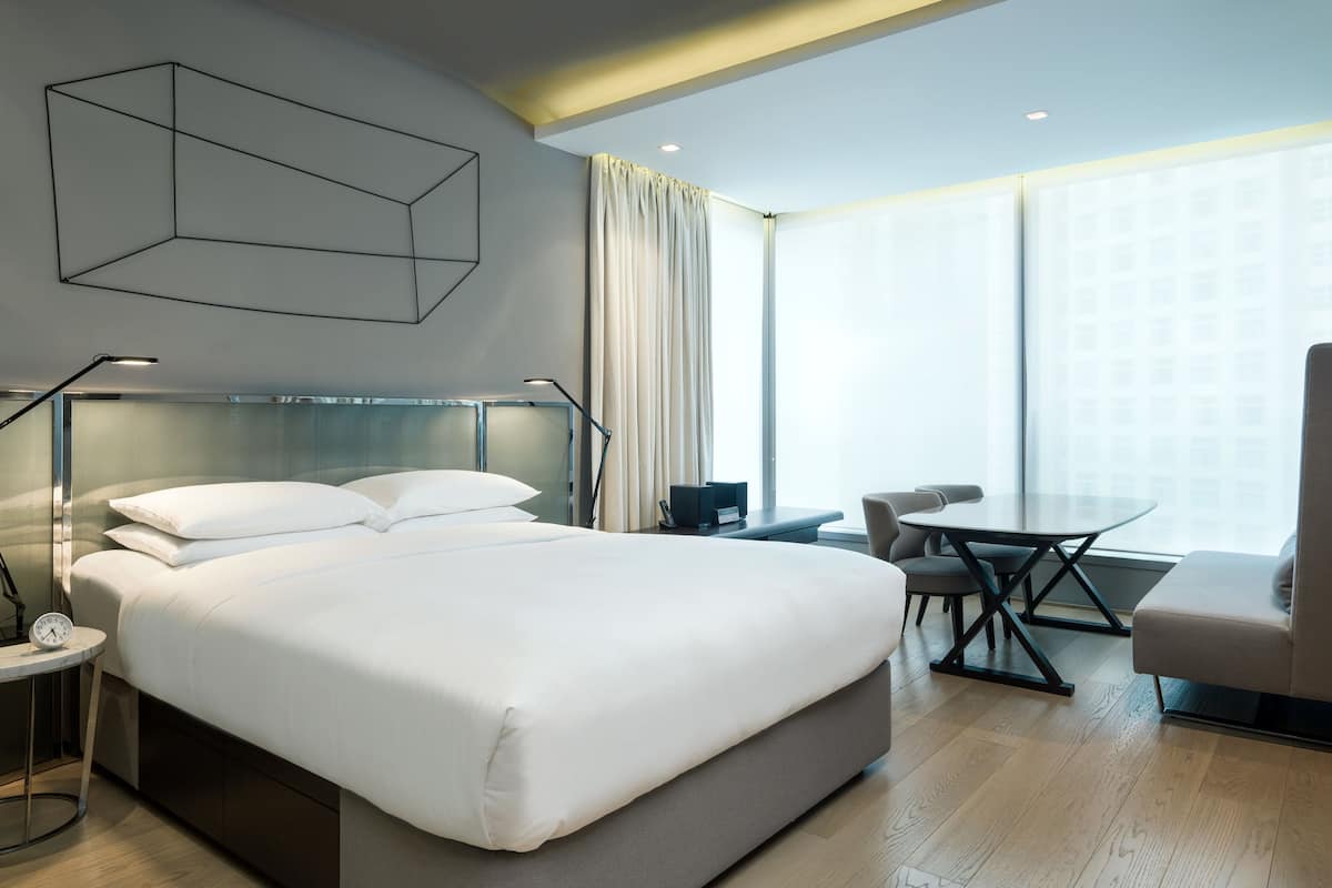 A modern hotel room with a large bed, bedside tables, a desk, and a chair.