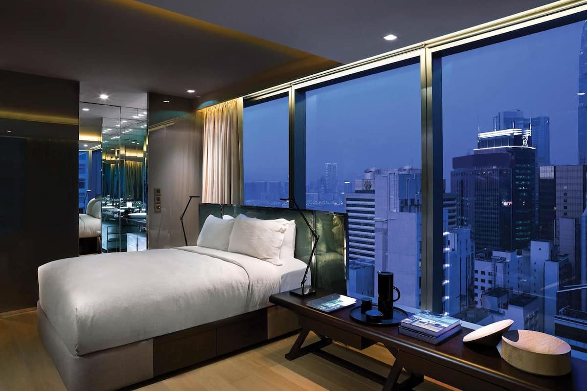 A modern hotel room with a large bed, a desk with a computer, and a view of a cityscape.