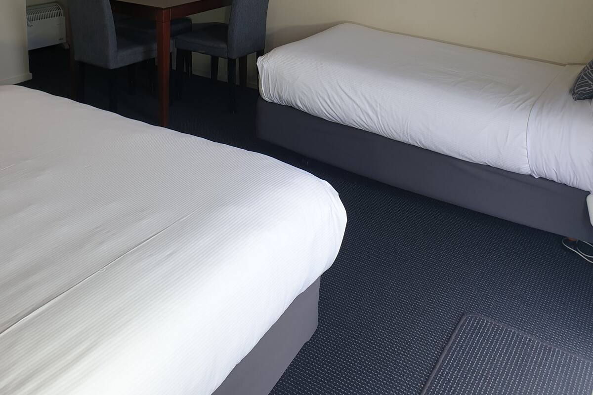 Ett hotellrum med två sängar, ett skrivbord, en stol och en tavla som föreställer en brygga i solnedgången.