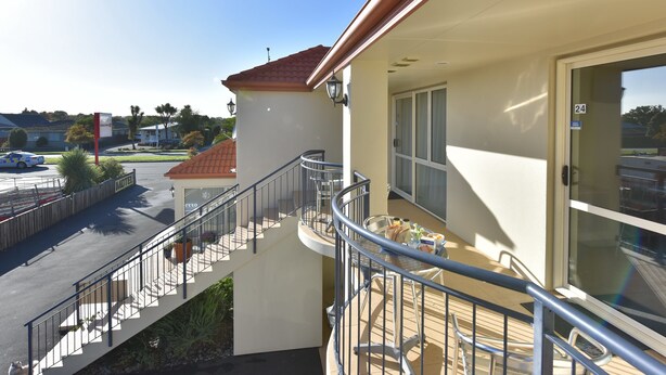 Ein Hotelbalkon mit Metallgeländer, einem Esstisch mit Stühlen und Blick auf die Straße sowie weitere Gebäude.