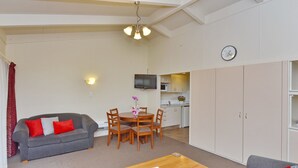 Ein gemütlicher Wohnraum mit grauem Sofa, einem Holzesstisch und einer Küchenzeile im Hintergrund.