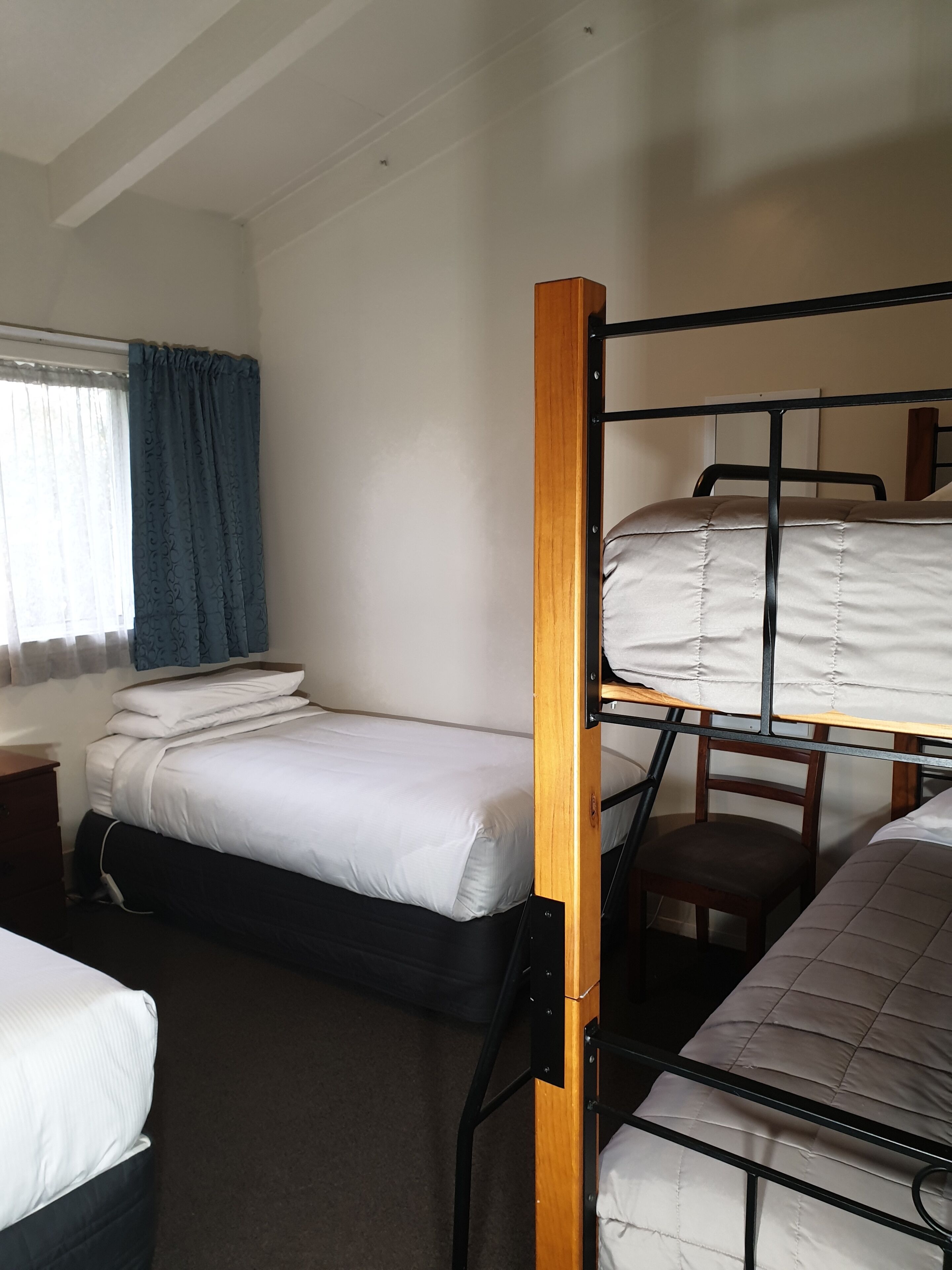 A bunk bed room with a window, curtains, and a desk.