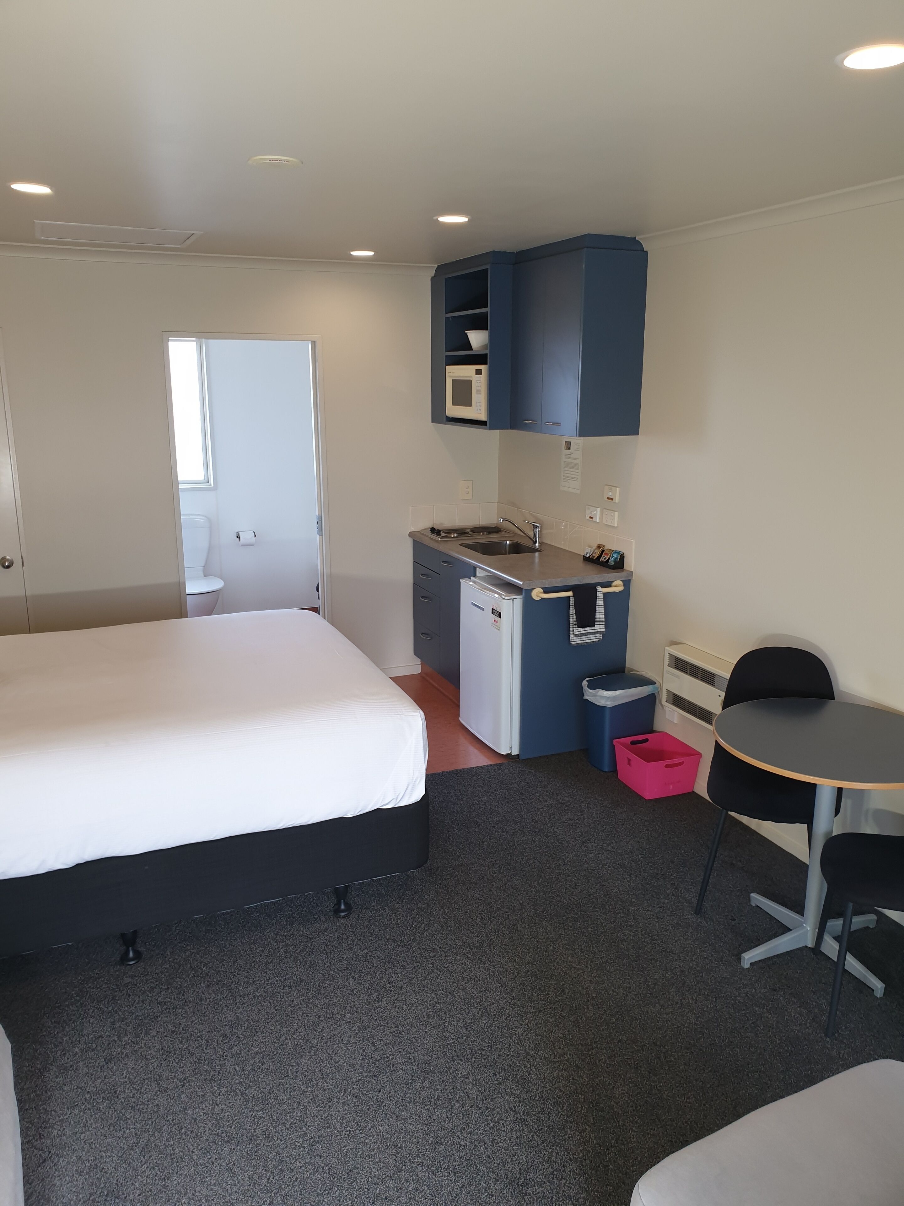 Een compacte hotelkamer met een eenpersoonsbed, een kleine kitchenette, een bureau en een stoel.
