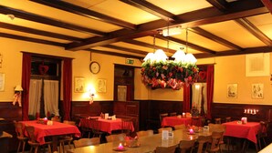 A restaurant with multiple tables covered in red tablecloths, wooden chairs, and hanging floral arrangements. - BasicRooms Hotel (Matten bei Interlaken)