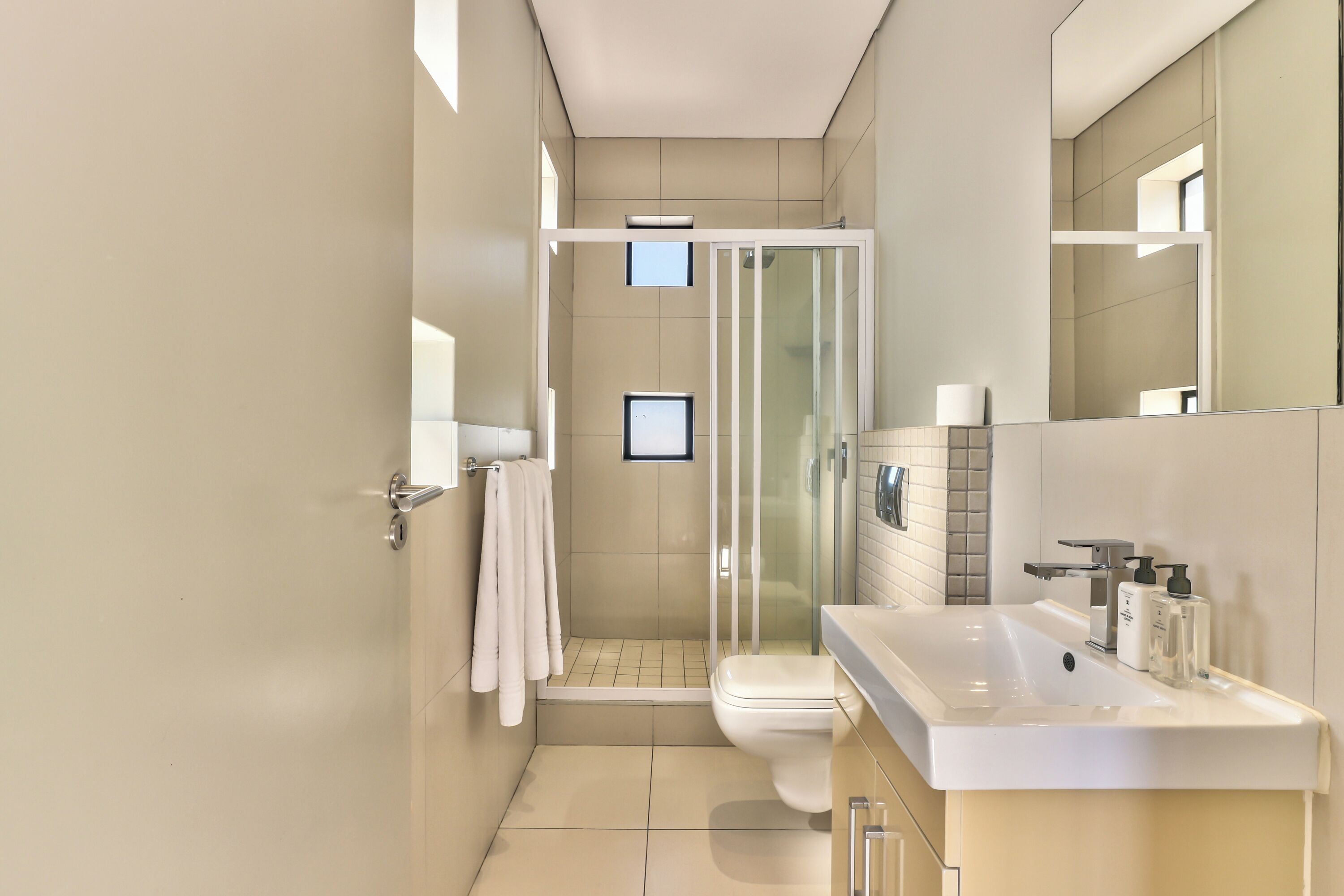 A modern bathroom with a shower, toilet, and sink, featuring a glass shower enclosure and a large mirror.