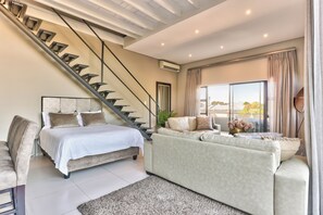 Un salon moderne avec un escalier, un lit, un canapé et une grande fenêtre donnant sur un beau paysage.