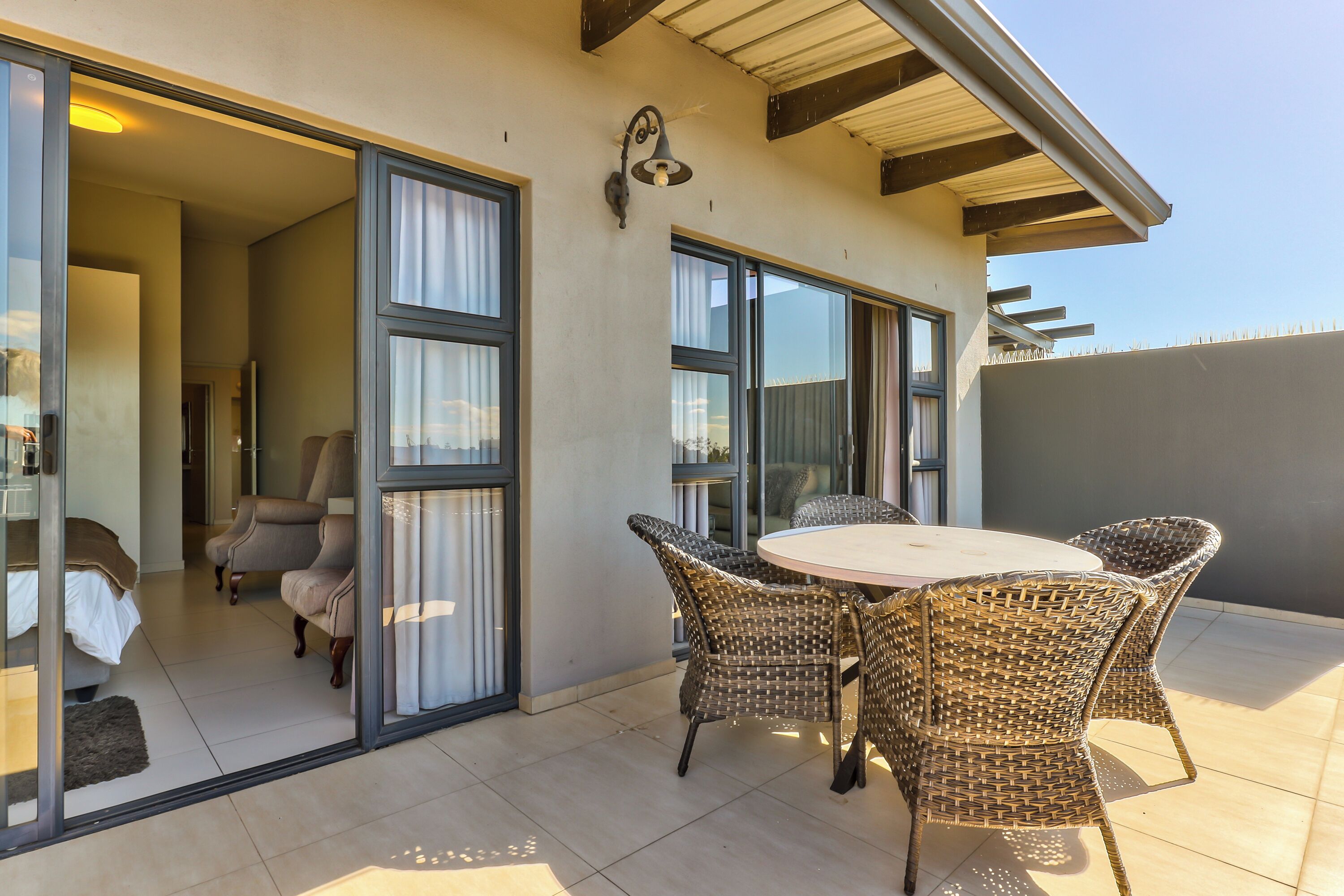 A patio with wicker chairs, a round table, and a sliding glass door leading to a bedroom.