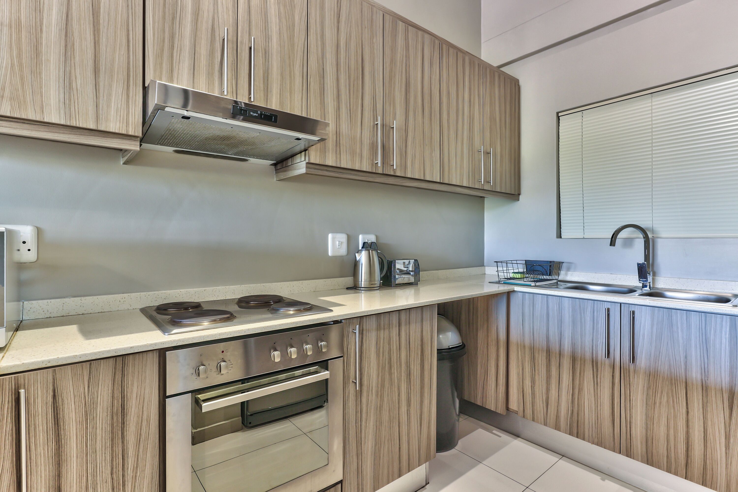 A modern kitchen with wooden cabinets, stainless steel appliances, and a window with blinds.