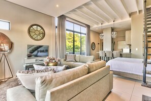 A modern living room with a large sofa, a television, and a dining area with chairs. - Heritage Square Apartments (Cape Town)