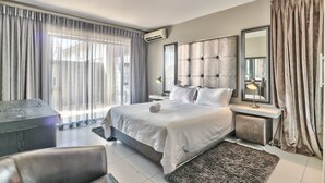 A modern bedroom with a large bed, a bedside table with a lamp, a mirror, and a view of the outdoors through sheer curtains. - Heritage Square Apartments (Cape Town)